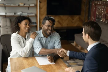 Three professionals, two men and one woman, shaking hands over a wooden table with documents.
